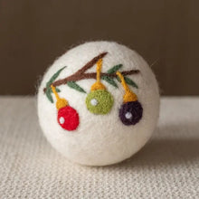 A white wool dryer ball with a branch holding holiday ornaments on it. 