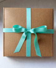 A square brown kraft paper gift box tied with a satin mint green ribbon in a bow, photographed from above on a light neutral background. 